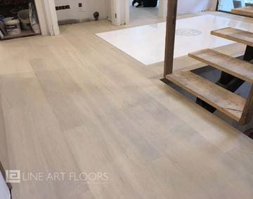 Light wood flooring with modern staircase in a bright room.