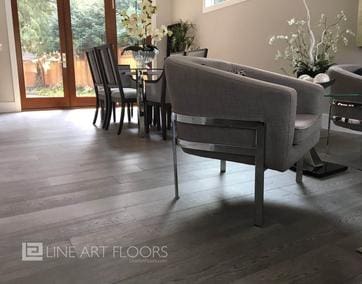 Modern living room with gray sofa and dining area featuring wood floors.